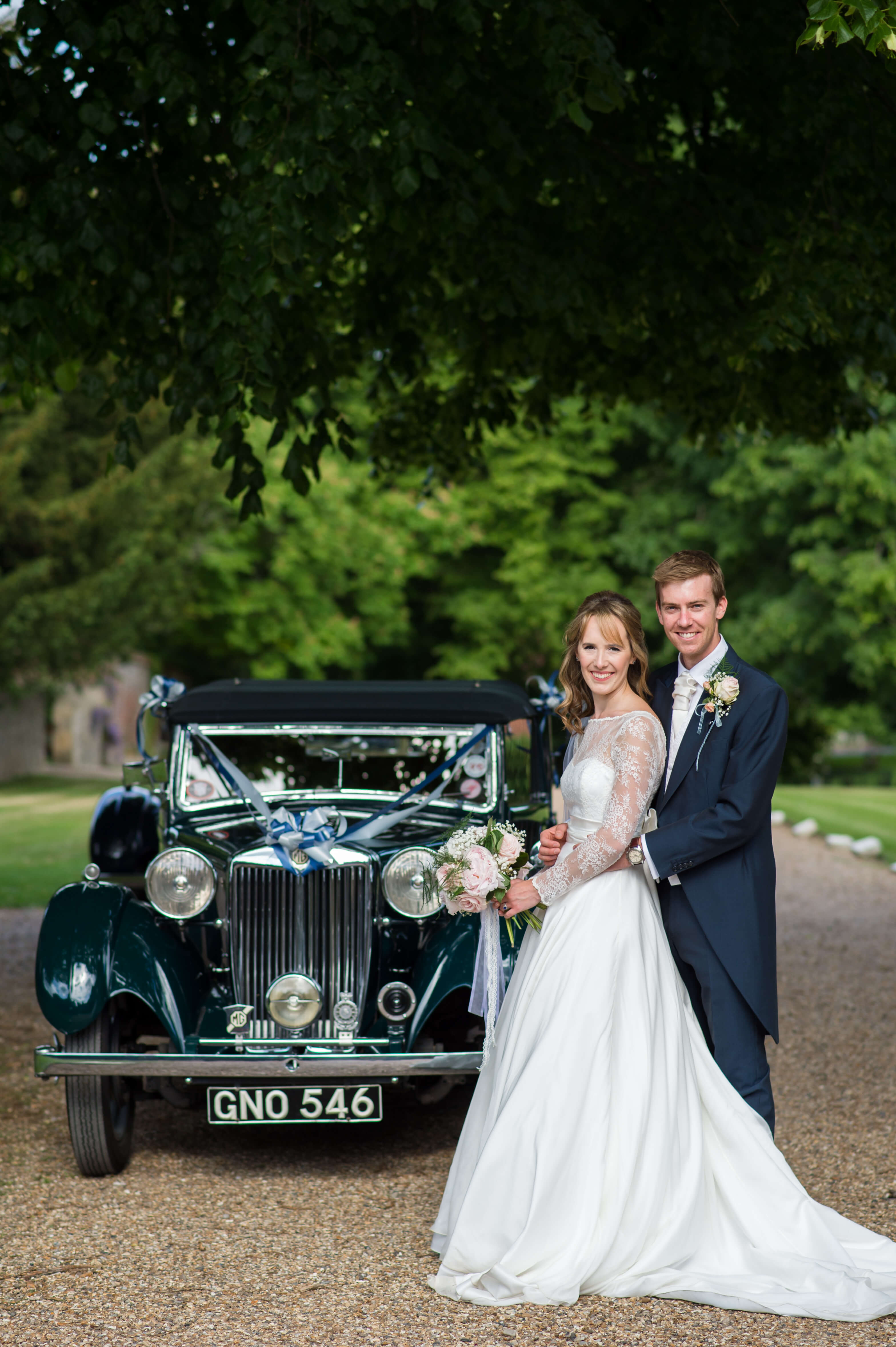 A wedding couple standing in front of a vintage car 